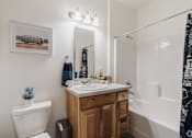Thumbnail 15 of 31 - A bathroom with a white toilet, a wooden vanity, and a shower with a black and white curtain.