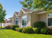 Thumbnail 1 of 3 - Side view of Oakstone Apartments leasing office with manicured green lawn and shrubbery lining the walls, while large, oversized windows look out into the grass at Oakstone Apartments in Clearview, UT