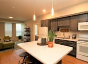 Thumbnail 20 of 33 - Modern kitchen island and open living area at Morrow Apartments in St. Paul, MN, featuring dark cabinetry