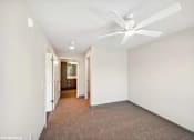 Thumbnail 25 of 40 - A room with a ceiling fan and carpeted floor.