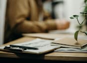 Thumbnail 10 of 10 - A person is sitting at a desk with a notebook and a pen in front of them.