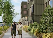 Thumbnail 5 of 10 - Two people walking down a sidewalk past a green building.