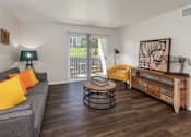 Thumbnail 22 of 37 - A living room with a grey couch, yellow pillows, a round table, and a wooden bench.