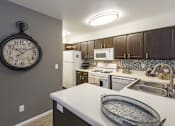 Thumbnail 11 of 37 - A kitchen with a white counter top and a large clock hanging on the wall.