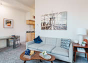 Thumbnail 9 of 29 - A living room with a grey couch, a coffee table, and a large picture of a bridge hanging on the wall.