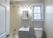 Thumbnail 8 of 12 - A bathroom with a white sink, toilet, and a mirror above a light switch.