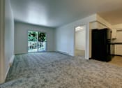 Thumbnail 8 of 17 - A spacious living room with a carpeted floor and a view of a fence and trees through a window.