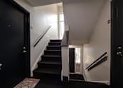 Thumbnail 22 of 28 - A staircase with a black carpeted runner and white risers.
