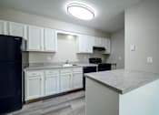 Thumbnail 6 of 28 - A kitchen with white cabinets and a black fridge.