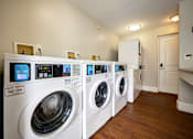 Thumbnail 46 of 55 - A row of white front load washing machines are lined up in a laundry room.