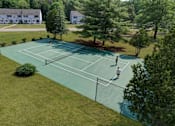 Thumbnail 26 of 33 - Two people playing tennis on a court with trees and houses in the background.