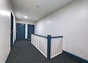 Thumbnail 16 of 23 - A hallway with a white railing and dark carpet.