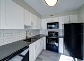 Thumbnail 3 of 47 - A black refrigerator sits in a kitchen with white cabinets and a black dishwasher.