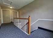 Thumbnail 19 of 25 - A hallway with a carpeted floor and a wooden railing.