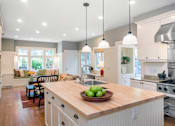 Thumbnail 19 of 20 - A modern kitchen with a wooden island and pendant lights.