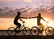 Thumbnail 2 of 2 - Two people riding bicycles on the beach at sunset.