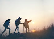 Thumbnail 5 of 30 - Three hikers with backpacks are silhouetted against the sunset.