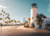 Thumbnail 20 of 30 - A white lighthouse with a black top stands in front of a building with a sign that reads