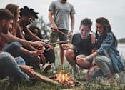 Thumbnail 2 of 8 - a group of people sitting around a campfire playing with a rope
