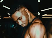 Thumbnail 1 of 6 - a man wearing a tank top and looking at his cell phone