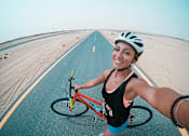 Thumbnail 2 of 6 - a woman riding a bike down a road on a beach