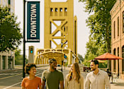 Thumbnail 8 of 14 - Four people walking down a sidewalk in front of a yellow structure with the words "NW 4th St" on it.