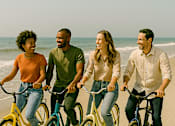 Thumbnail 3 of 14 - Four people riding bikes on a beach.