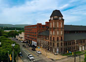 Thumbnail 5 of 8 - A large red brick building with a clock tower sits on a street corner.