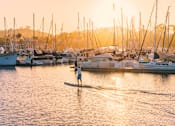Thumbnail 9 of 12 - a man paddle boarding in a marina at sunset