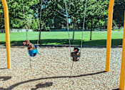 Thumbnail 2 of 8 - Two children playing on swings in a playground.