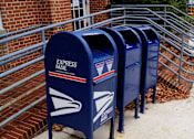 Thumbnail 7 of 11 - A row of blue mailboxes are lined up on a sidewalk.