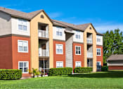 Thumbnail 6 of 11 - A red and beige apartment building with a green lawn in front.