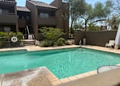 Thumbnail 5 of 21 - A swimming pool in a backyard with a brown fence and a white chair.