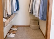Thumbnail 7 of 38 - A small closet with clothes hanging and shoes on the floor.