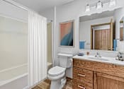 Thumbnail 8 of 12 - A white toilet sits in a bathroom with a wooden vanity and a mirror.