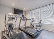 Thumbnail 28 of 47 - A home gym with a treadmill, elliptical trainer, and a television.