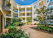 Thumbnail 18 of 33 - A courtyard with a tree and potted plants in front of apartment buildings.
