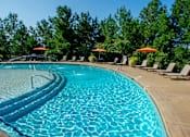 Thumbnail 14 of 33 - A large swimming pool surrounded by trees and lounge chairs.