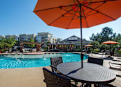 Thumbnail 8 of 33 - A patio with a table and chairs under an orange umbrella.