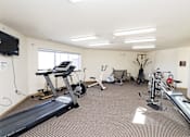 Thumbnail 20 of 22 - A spacious gym with a variety of equipment including treadmills, stationary bikes, and a television.