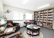 Thumbnail 3 of 22 - A living room with a leather couch, a coffee table, and a bookshelf filled with books.