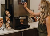 Thumbnail 14 of 26 - a woman is reaching for a coffee machine in a coffee shop