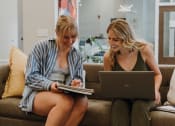 Thumbnail 16 of 26 - two women sitting on a couch looking at a laptop computer