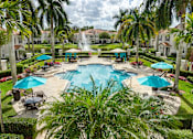 Thumbnail 2 of 17 - A pool surrounded by palm trees and umbrellas.