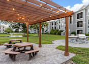 Thumbnail 10 of 22 - A wooden pergola with string lights is over a picnic table in a courtyard.