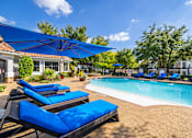 Thumbnail 10 of 22 - A pool area with blue lounge chairs and umbrellas.