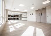 Thumbnail 10 of 20 - A spacious room with wooden floors and white walls, featuring a large window on the left and a glass door in the center.
