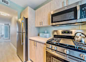 Thumbnail 12 of 14 - A kitchen with a stove, refrigerator, and microwave.