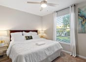 Thumbnail 18 of 22 - A bedroom with a large bed, a ceiling fan, and a window with white curtains.