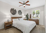 Thumbnail 22 of 30 - A bedroom with a bed, a nightstand with a lamp, a ceiling fan, and two wall decorations.